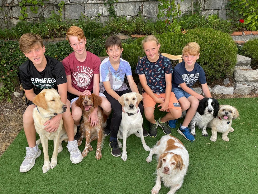 5 enfants et leurs chiens assis sur un banc sourient, joyeux, à l'objectif